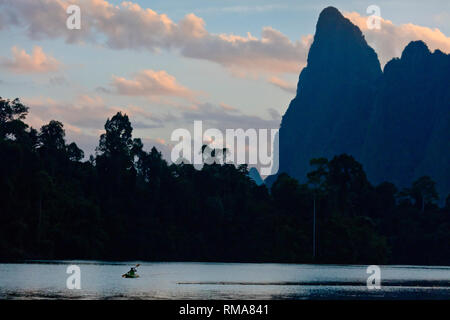 Kajak bei Sonnenaufgang unter KARST Formationen, die sich aus der CHEOW LAN LAKE - Khao Sok Nationalpark, THAILAND Stockfoto