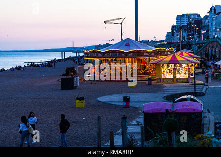 Brighton, Großbritannien - Juni 2018 Menschen entspannend auf dem Kies Sand Strand von Brighton in England. Kinder reiten das Karussell im Vergnügungspark mit Spielzeug Stände. Stockfoto