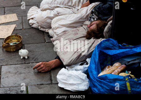 BIRMINGHAM, UK - März 2018 Rough Sleeper Liegend auf kalten Pflaster mit seinen Habseligkeiten. Sparschwein neben Blechdose für Geld, das er von Passersb Stockfoto