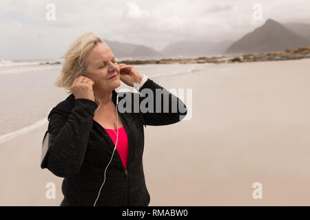 Gerne ältere Frau Musik hören über Kopfhörer am Strand Stockfoto