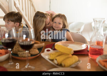 Mutter küssen ihre Tochter am Esstisch Stockfoto