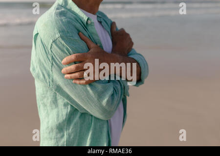 Älterer Mann, der mit den Armen am Strand gekreuzt Stockfoto