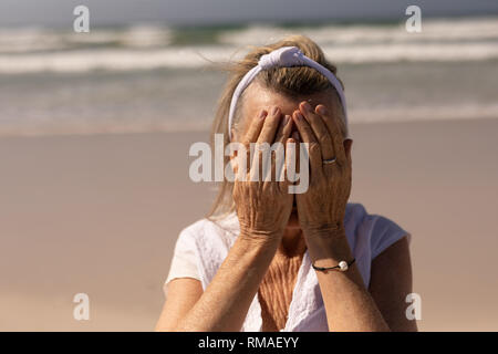 Vorderansicht der älteren Frau, die ihr Gesicht beim Stehen auf dem Strand Stockfoto