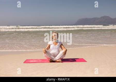 Vorderansicht der älteren Frau, Meditieren am Strand an einem sonnigen Tag Stockfoto
