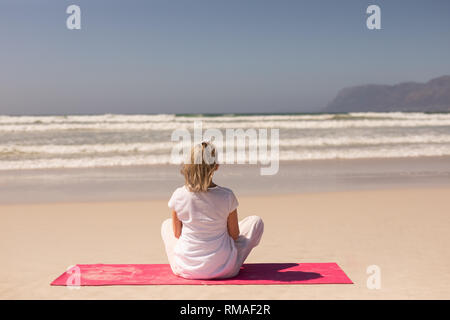 Rückansicht Senior Frau Meditation am Strand an einem sonnigen Tag Stockfoto