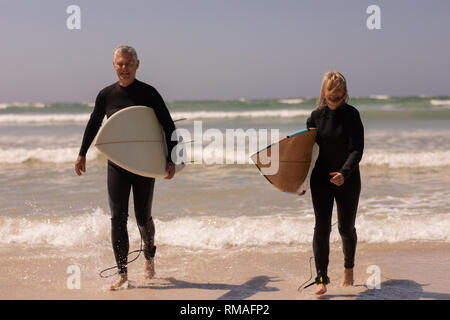 Senior Paar mit Surfbrett zu Fuß am Strand. Stockfoto