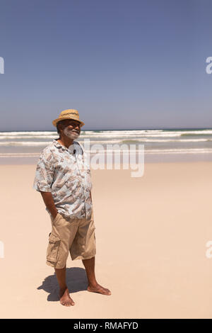 Älteren schwarzen Mann mit Hut und die Hände in der Tasche stehen am Strand. Stockfoto