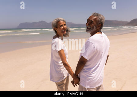 Gerne älteres Paar Hände halten und mit Blick auf die Kamera am Strand Stockfoto