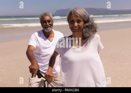 Senior Paar steht mit dem Fahrrad und der Kamera am Strand Stockfoto