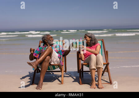 Senior Paar relaxen im Liegestuhl und Toasten cocktail Gläser am Strand Stockfoto
