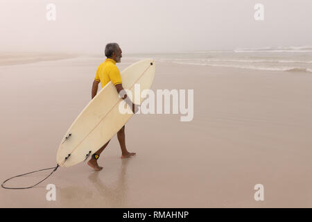 Ältere männliche Surfer gehen mit Surfbrett am Strand Stockfoto