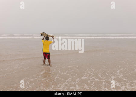 Ältere männliche Surfer mit dem Surfbrett auf dem Kopf Stockfoto