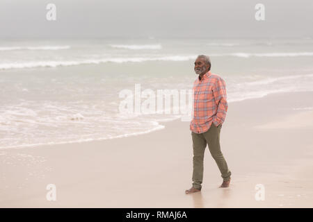 Gerne älterer Mann mit Händen in der Tasche zu Fuß am Strand Stockfoto