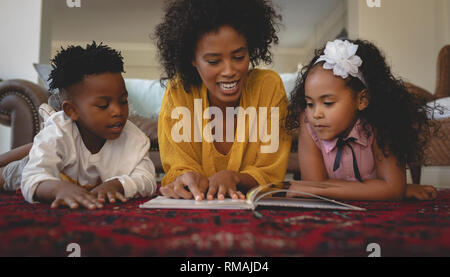 Afrikanische amerikanische Mutter mit ihren niedlichen Kinder liegen auf dem Boden und Lesen ein storybook Stockfoto