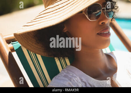 Afrikanische amerikanische Frau mit Hut und Sonnenbrille relaxen im Liegestuhl in Ihrem Hinterhof Stockfoto