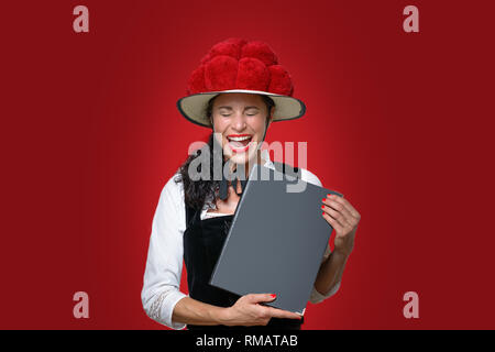 Ehrliches Porträt eines Lachen attraktive junge Schwarzwald Kellnerin Holding ein Menü in traditioneller Kleidung mit Bollenhut mit Rot gekleidet Stockfoto