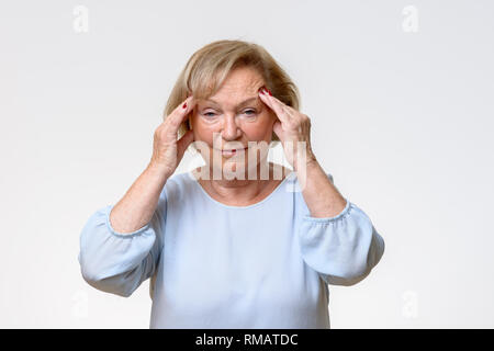 Ältere Frau in einer schweren Kopfschmerzen ihre schläfen Reiben mit den Fingern mit einem Ausdruck des Schmerzes auf ihrem Gesicht Stockfoto