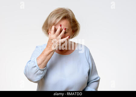 Ältere Frau, die ihr Gesicht mit der Hand, als sie versucht, ihre Gefühle in der Nähe zu sehen, isoliert auf Hellgrau zu verbergen Stockfoto