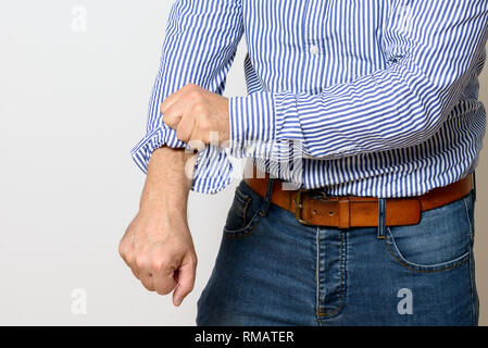 Im mittleren Alter Mann rollt die Ärmel seiner gestreiften blaues und weißes Hemd in einer Nahaufnahme 7/8 Blick auf Weiß mit Kopie Raum Stockfoto