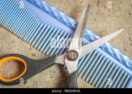 Eine Schere und einen blauen Kamm gehalten auf einem grauen Holz- strukturierte Tabelle Ansicht von oben. Stockfoto