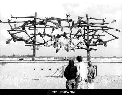 Internationalen Mahnmal von Nandor Glid auf dem ehemaligen Appellplatz des Konzentrationslagers Dachau. Im Hintergrund, camp Kasernen, sowie der Todesangst-Christi Kapelle Dachau am Ende des Lagers Straße. Stockfoto