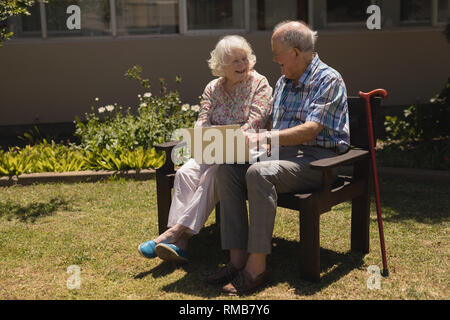 Vorderansicht des Senior Paar sitzt auf der Bank und mit Laptop im Garten Stockfoto