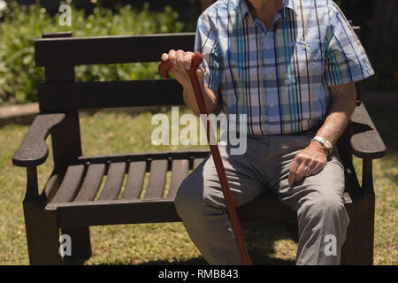 Älterer Mann sitzend mit Stock auf der Werkbank Stockfoto