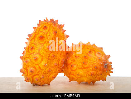 Zwei ganze Kiwano Obst, auch bekannt als Cucumis metuliferus, gehörnten Melone, oder Afrikanische gehörnten Gurke sitzen auf Holz Tisch auf Weiß isoliert. Kiwano ist Stockfoto