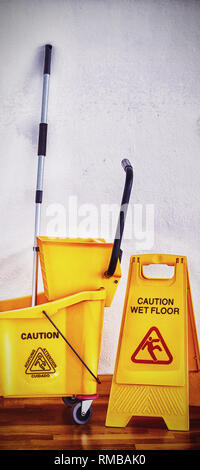 Gelbes Schild mit Mop Schaufel am Boden gegen die Wand Stockfoto