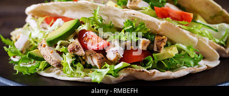 Pita-brot-Sandwiches mit gegrilltem Hähnchenfleisch, Avocado, Tomate, Gurke und Salat serviert auf Holz- Hintergrund. Close Up. Gesundes fast food conce Stockfoto