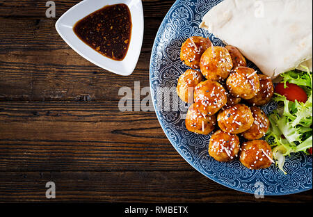 Fleischbällchen in süß und sauer auf einem Teller mit pita Brot und Gemüse Glasur im marokkanischen Stil auf einem Holztisch. Tapas. Trend essen. Ansicht von oben Stockfoto