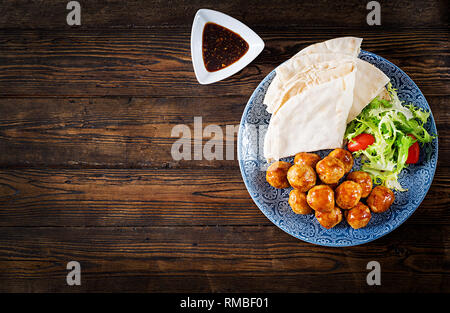 Fleischbällchen in süß und sauer auf einem Teller mit pita Brot und Gemüse Glasur im marokkanischen Stil auf einem Holztisch. Tapas. Trend essen. Ansicht von oben Stockfoto