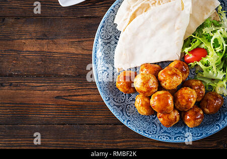 Fleischbällchen in süß und sauer auf einem Teller mit pita Brot und Gemüse Glasur im marokkanischen Stil auf einem Holztisch. Tapas. Trend essen. Ansicht von oben Stockfoto