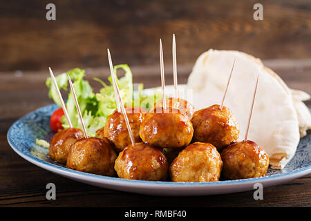 Fleischbällchen in süß und sauer auf einem Teller mit pita Brot und Gemüse Glasur im marokkanischen Stil auf einem Holztisch. Tapas. Trend essen. Stockfoto