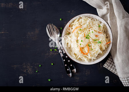 Fermentierter Kohl. Veganes essen. Sauerkraut mit Karotte und Gewürzen in der Schüssel auf dem dunklen Hintergrund. Trend essen. Ansicht von oben. Flach, kopieren Raum Stockfoto