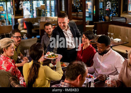 Reifen Kellner, eine Platte von Lebensmitteln über zu einer Frau sitzt und eine kleine Gruppe von Freunden. Stockfoto