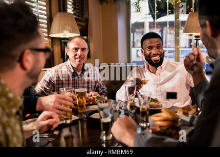 Kleine Gruppe von Mitte der erwachsenen männlichen Freunde genießen einige Essen in einem Restaurant. Sie reden und genießen jede andere Firma. Stockfoto
