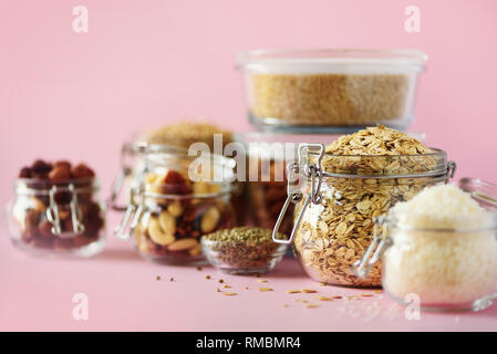 Vegane Ernährung über rosa Hintergrund mit kopieren. Nüsse, Samen, Getreide, Körner, die in Gläsern. Antioxidantien, Omega 3, Eiweiß und Ballaststoffe c Stockfoto