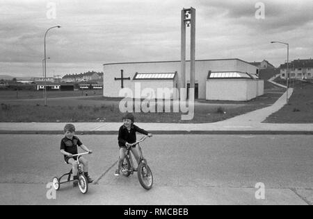 1970s irische Kinder, die draußen auf ihren Fahrrädern spielen. Limerick, in County Limerick, Irland. Westküste von Südiland 70s. Die neu erbaute Holy Family Church im O'Malley Park, Limerick, Teil des Anwesens Southill. HOMER SYKES. Stockfoto