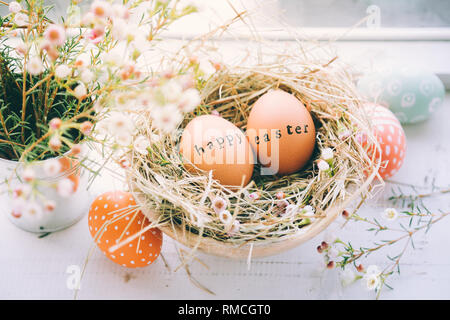 Ostereier mit Stempel Frohe Ostern gruss Text in einem Heu- und Blumen Nest neben einem Fenster zu Hause Stockfoto