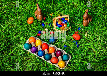 Schokolade Osterhasen, Stroh Korb voll bunter Eier auf grünem Gras Stockfoto