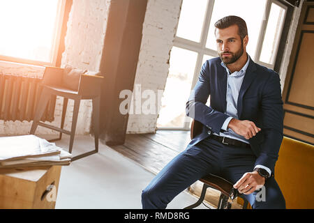 Immer perfekt... charmant und angenehm und bärtigen Geschäftsmann im eleganten Anzug im Sessel sitzt und nachdenklich. Mode suchen. Busine Stockfoto