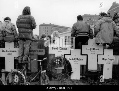 Kreuze zum Gedenken an die Opfer der Berliner Mauer, 1989. Hinter, eine Versammlung von Menschen kurz nach dem Fall der Berliner Mauer in der Bernauer Straße an der Kreuzung. Auf die Kreuze sind die folgenden Namen: Ida Siekmann, Bernd Luenser, Rudolf Urban, Ernst Mund, Olga Segler. Stockfoto