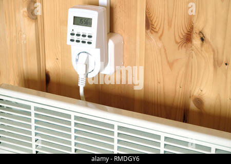Arbeiten weiß elektrischer Konvektor Heizung angeschlossen, um timer Steckdose im Smart house System gegen hölzerne Wand im Zimmer Seitenansicht closeup betrieben Stockfoto