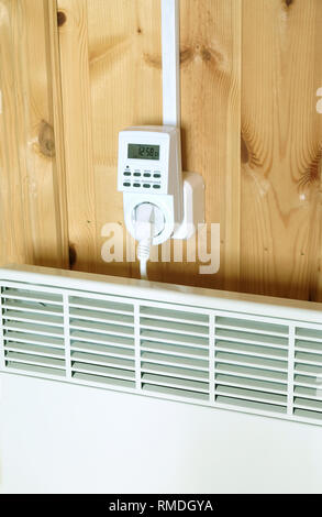 Arbeiten weiß elektrischer Konvektor Heizung angeschlossen, um timer Steckdose im Smart house System gegen hölzerne Wand im Zimmer Seitenansicht closeup betrieben Stockfoto