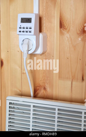 Arbeiten weiß elektrischer Konvektor Heizung angeschlossen, um timer Steckdose im Smart house System gegen hölzerne Wand im Zimmer Seitenansicht closeup betrieben Stockfoto