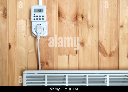 Arbeiten weiß elektrischer Konvektor Heizung angeschlossen, um timer Steckdose im Smart house System gegen hölzerne Wand im Zimmer Frontansicht betrieben Stockfoto