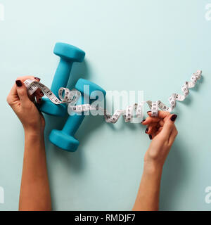 Weibliche Hand, Maßband, Hanteln über blauen Hintergrund. Ansicht von oben, flach. Gewicht verloren, Sport, Fitness, Ernährung Konzept. Banner mit Kopie sp Stockfoto