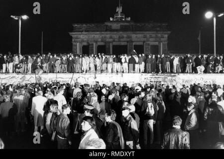 Kurz nachdem die Mauer geöffnet wurde, eine Masse von Menschen steht an der Wand, vor dem Brandenburger Tor und der Berliner Mauer. Es ist Nacht. Stockfoto