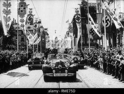 Adolf Hitler in seinem Mercedes, von einer begeisterten Bevölkerung gefeiert. Links und rechts der Straße mit NS-Fahnen, einschließlich der Flagge des Nationalsozialistischen Krieg Opferbetreuung neben einer Hakenkreuzfahne geschmückt. Stockfoto